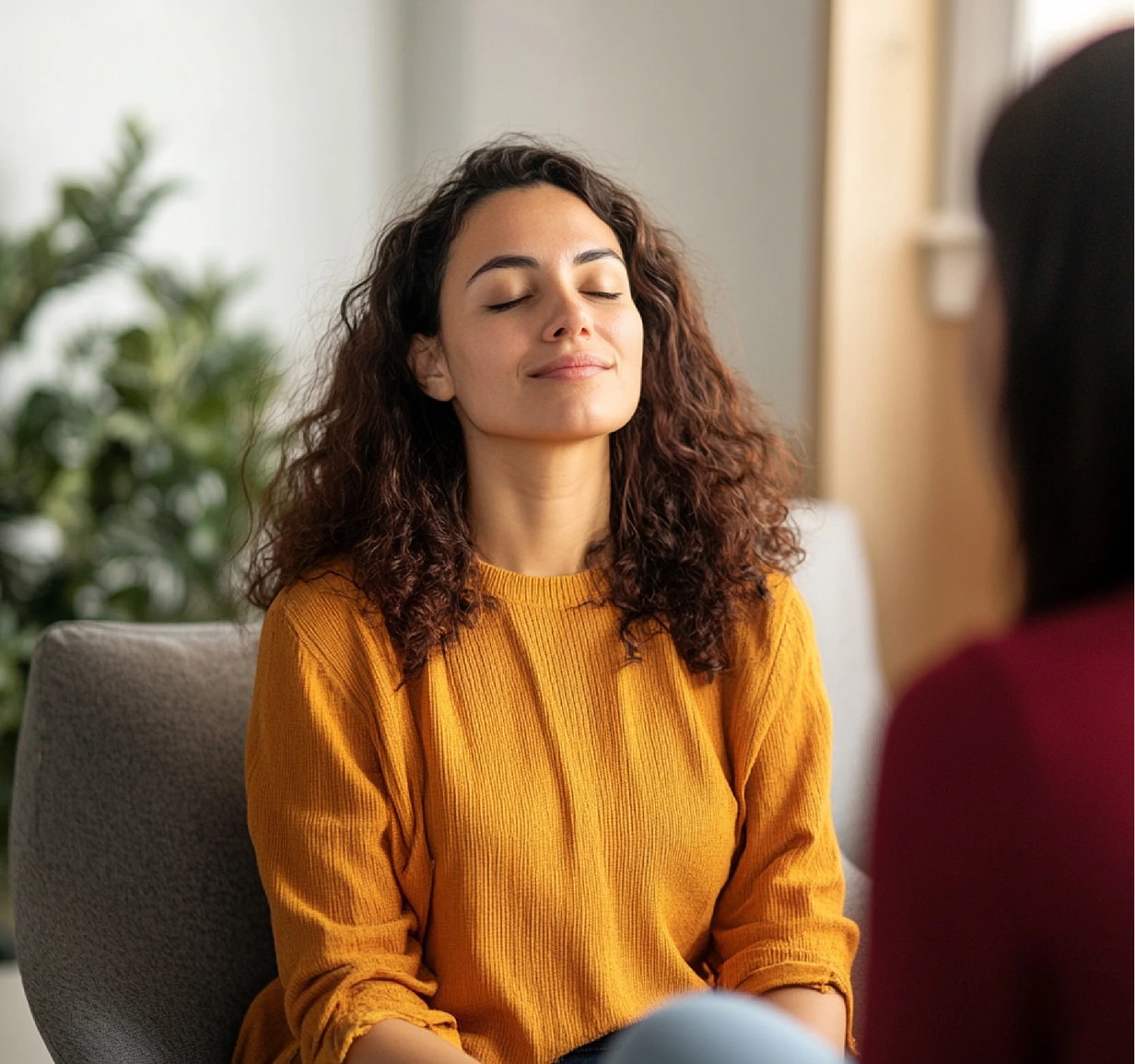 Woman in yellow sweater sitting with eyes closed in relaxed pose near plant