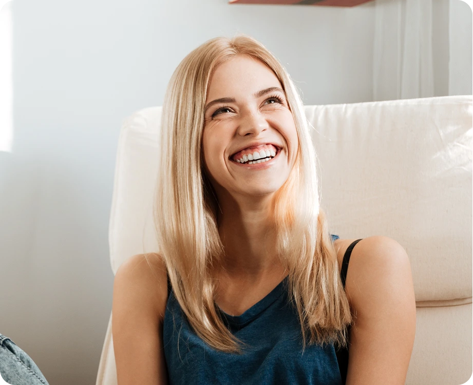 Woman with blonde hair smiling while sitting on couch in home setting