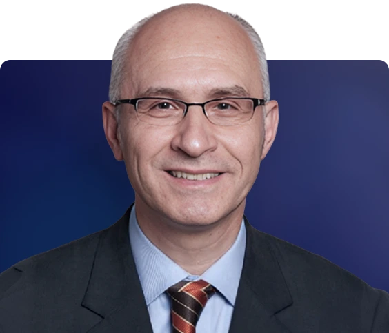Dr. Dragos, wearing glasses and a dark suit with striped tie, smiling at camera against blue background