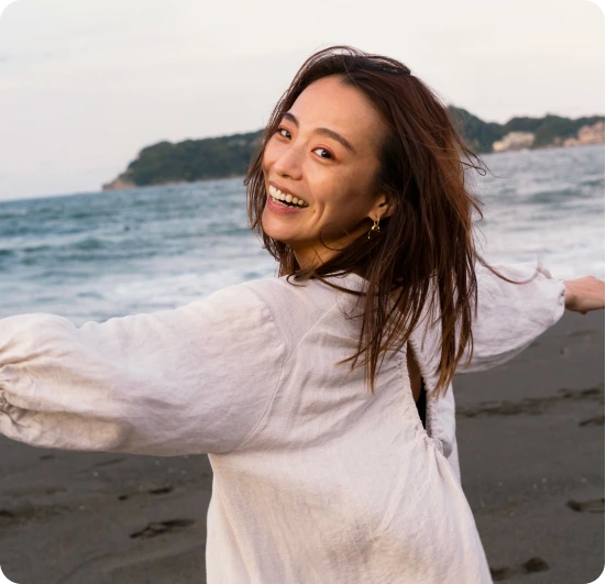 Smiling woman with arms outstretched on a beach at sunset