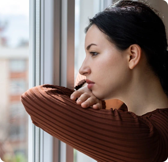 Woman with hand to face looking out window, expressing sadness or concern