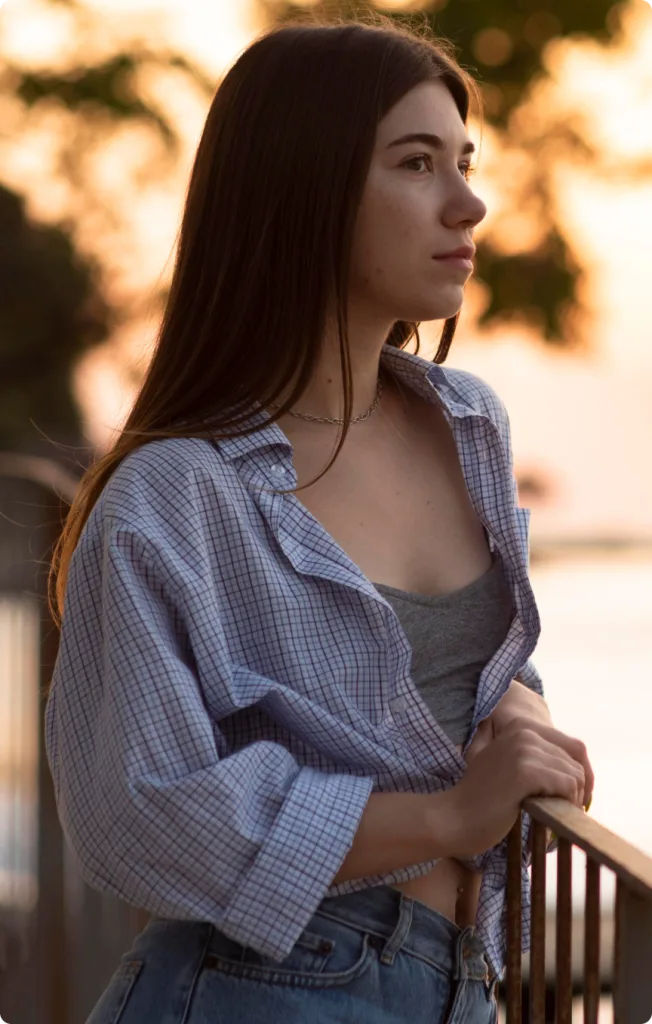 Woman in blue checkered shirt looking thoughtfully into the distance at golden hour