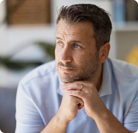 Man in a light blue shirt resting his chin on his hands, looking thoughtfully into the distance