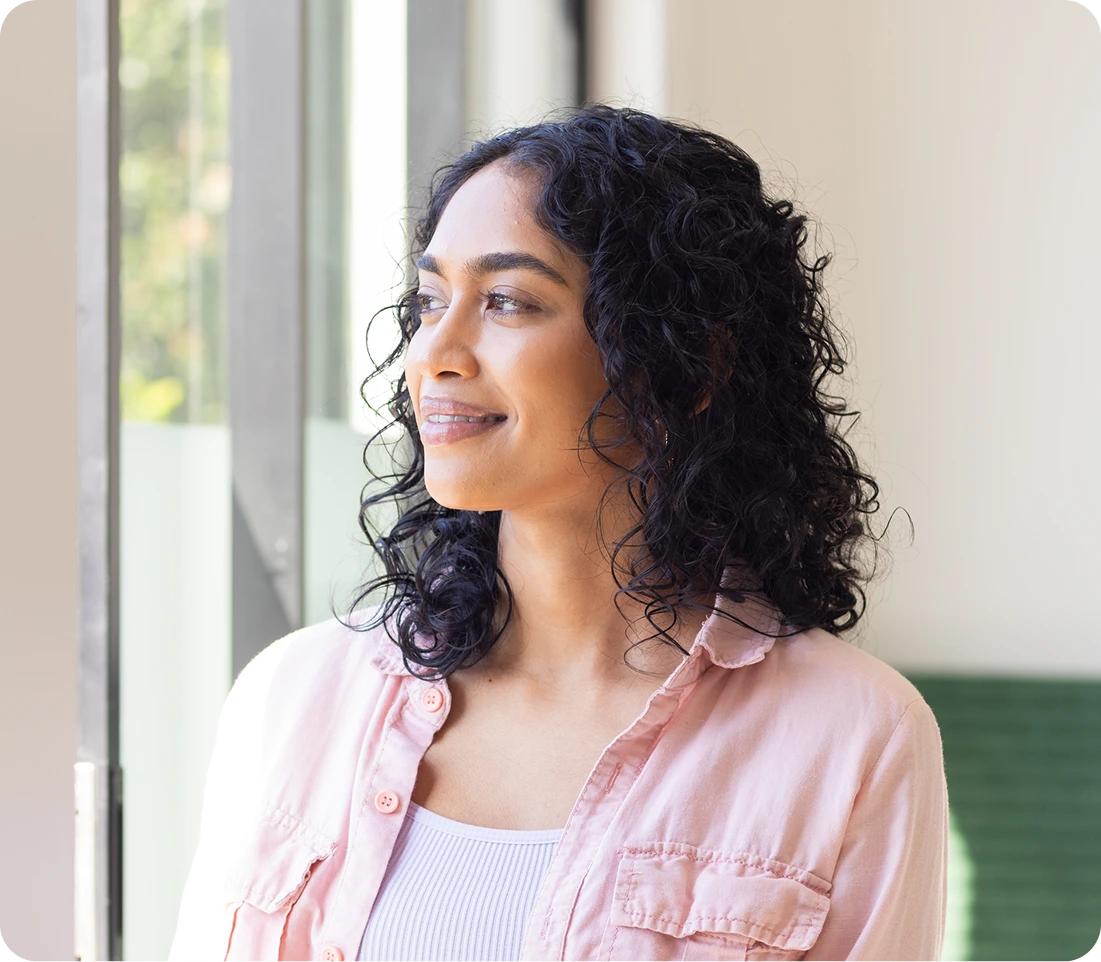 Woman smiling peacefully by a window, representing wellness and mental health treatment