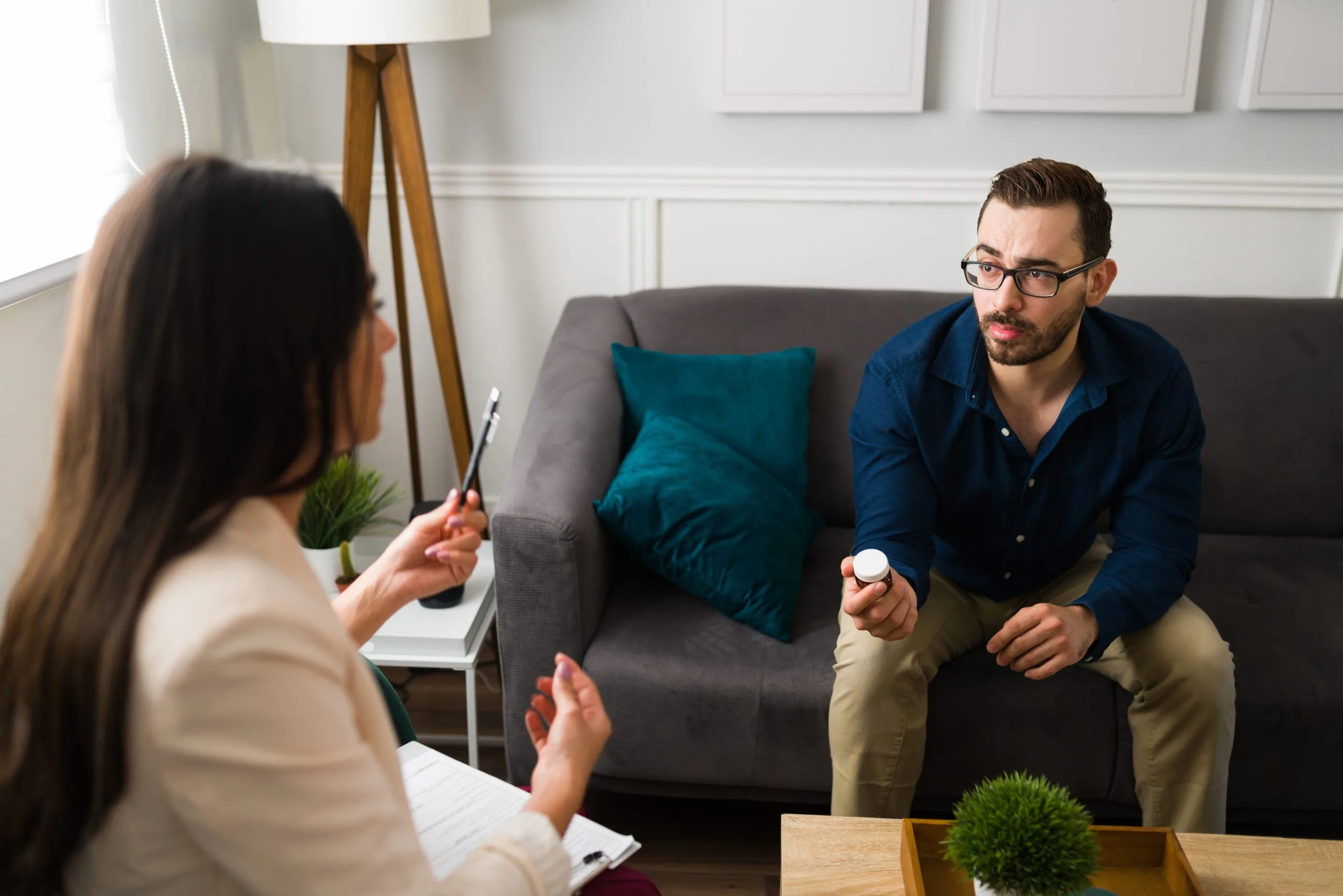 Therapist taking notes while speaking with male patient on gray couch in bright office