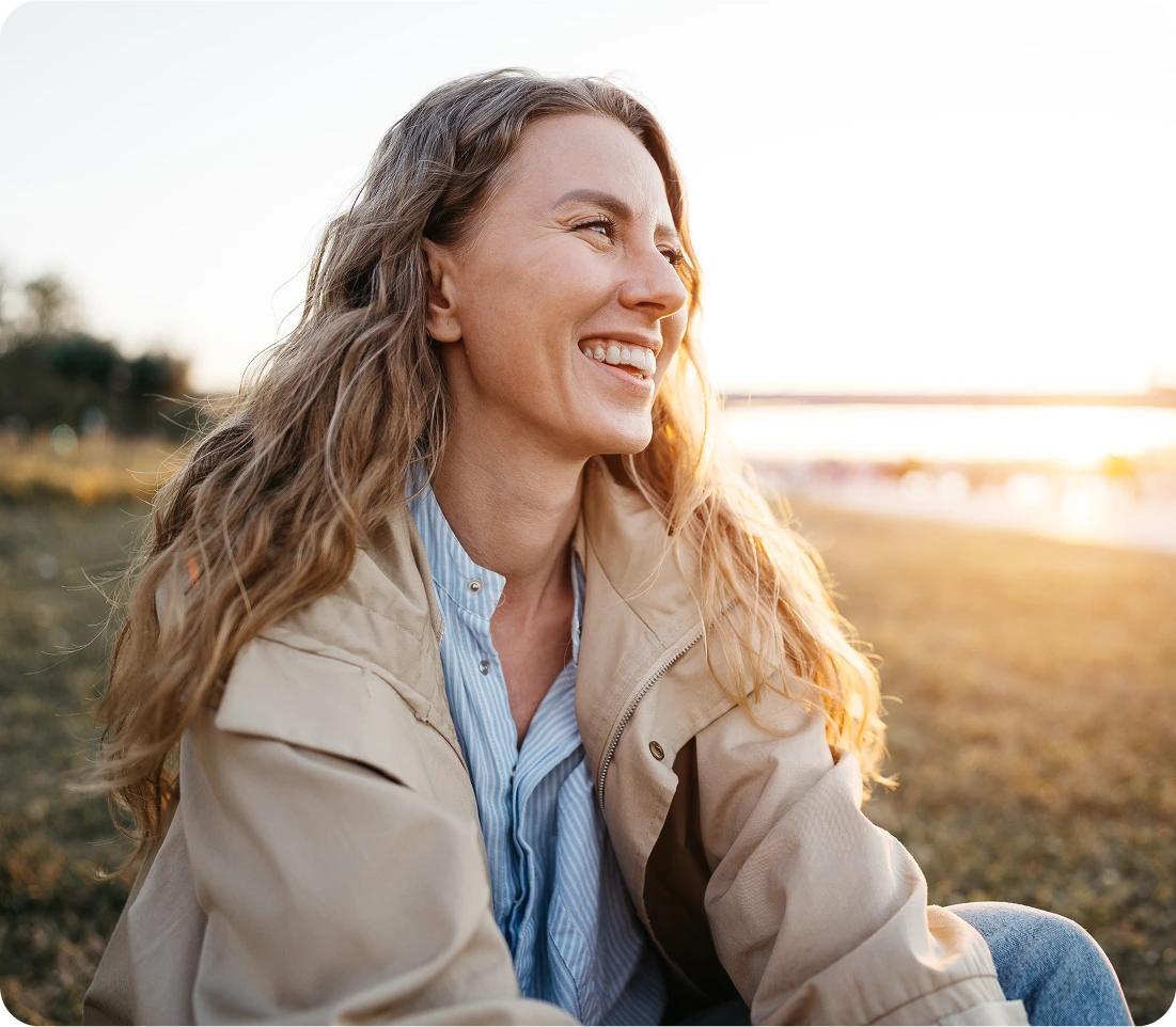 Woman smiling outdoors at sunset, appearing calm and content