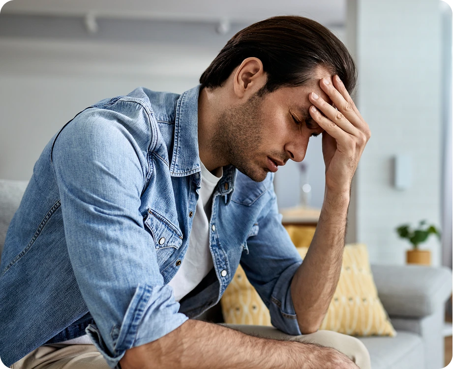 Man in denim shirt sitting with head in hand, showing signs of stress or anxiety