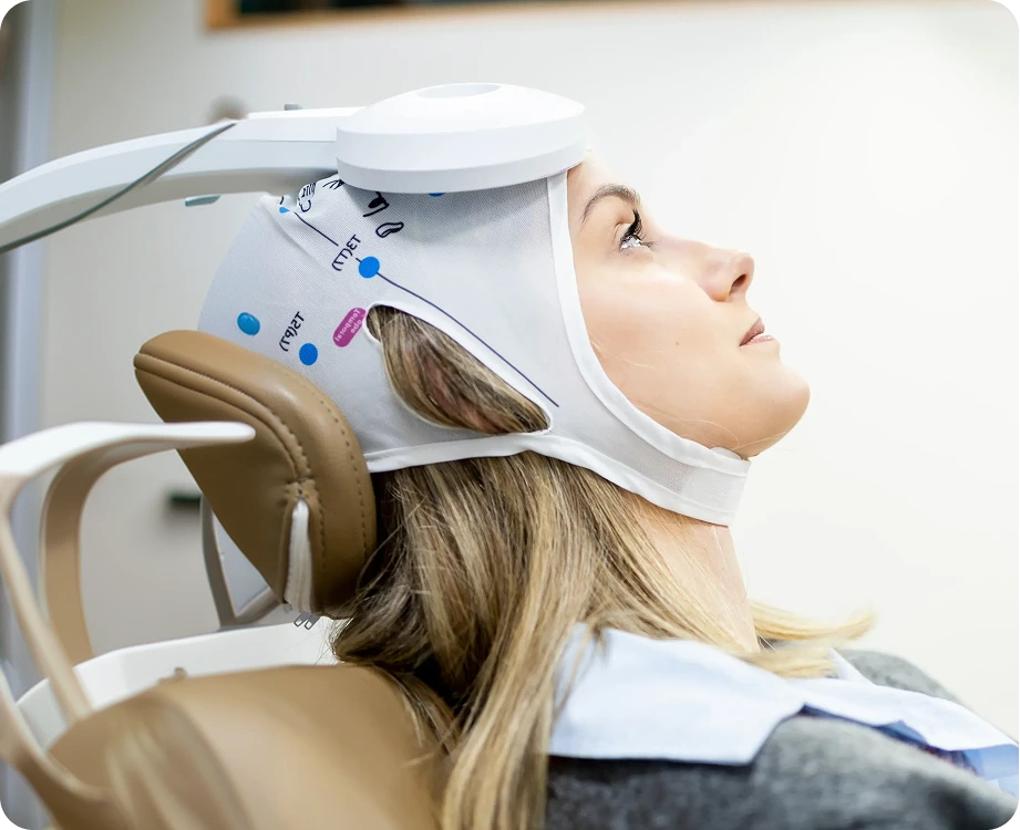 Patient receiving SAINT TMS treatment with white helmet device positioned on head