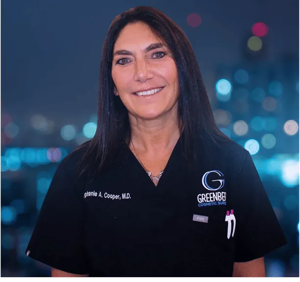 Jeannie A. Cooper, M.D. in black Greenberg Cosmetic Surgery scrubs against cityscape background