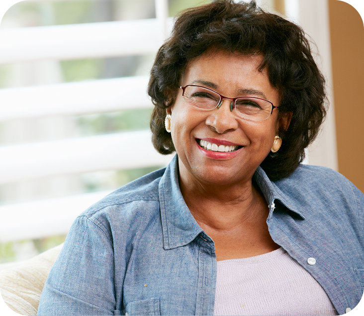 Woman wearing glasses smiling indoors near window with blurred shelving