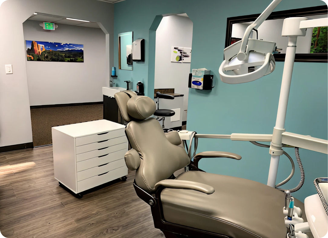 Dental treatment room with beige patient chair, overhead light, white cabinets, and turquoise walls