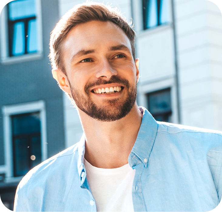 Man in light blue shirt smiling outdoors in front of modern building