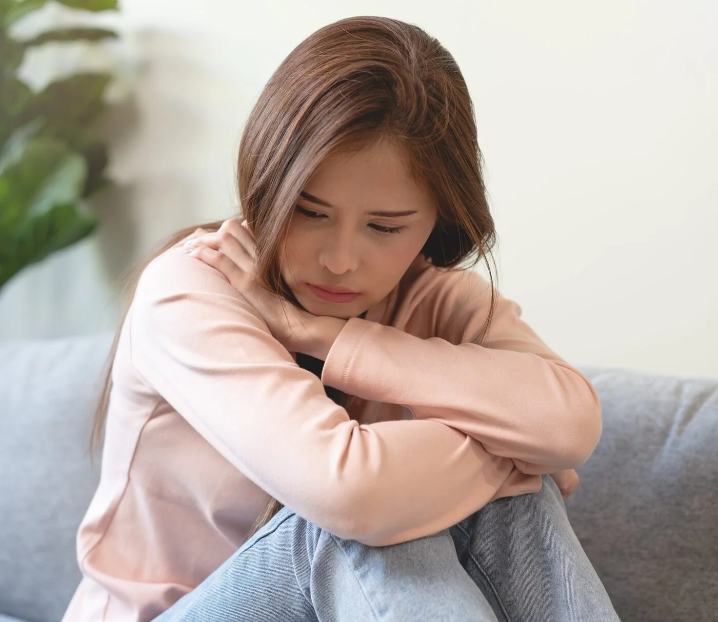 Young woman sitting on a couch, hugging her knees
