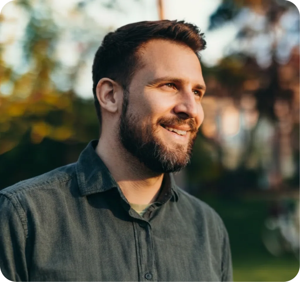 Man smiling outdoors in natural light wearing a dark button-up shirt