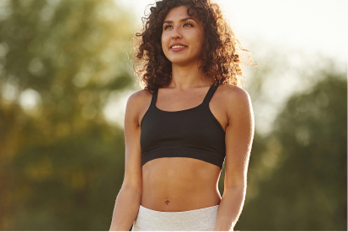 Woman in black sports bra looking upward outdoors with blurred green background