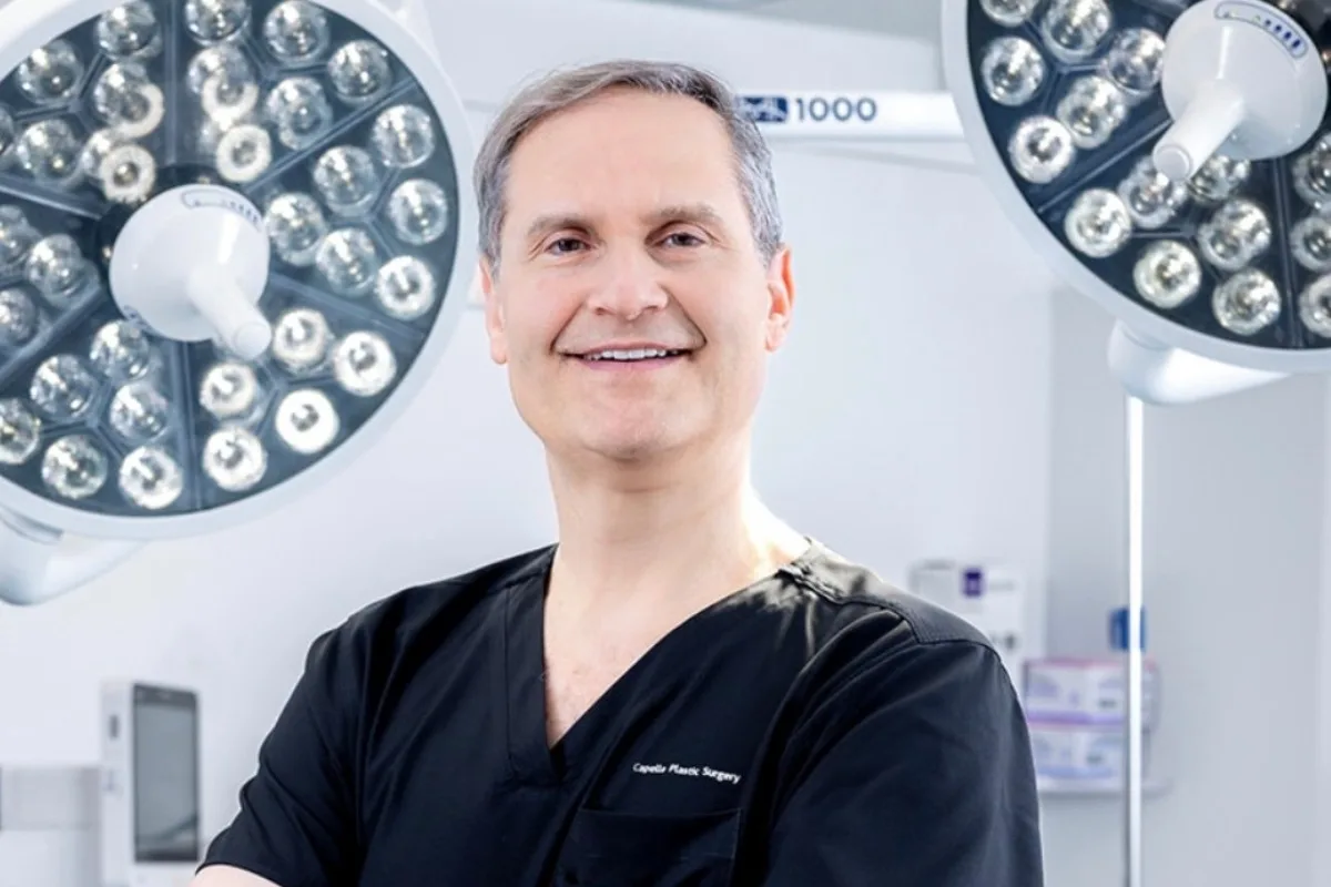 Surgeon in black scrubs smiling in operating room under surgical lights