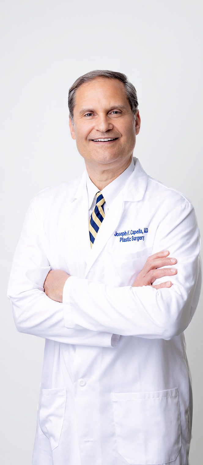 Dr. Joseph F. Capella, MD in white coat with arms crossed, smiling at camera