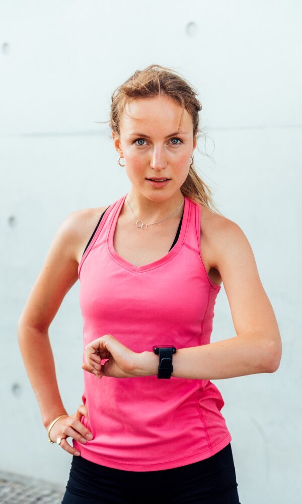 Woman in pink sports tank top wearing smartwatch, standing against light background