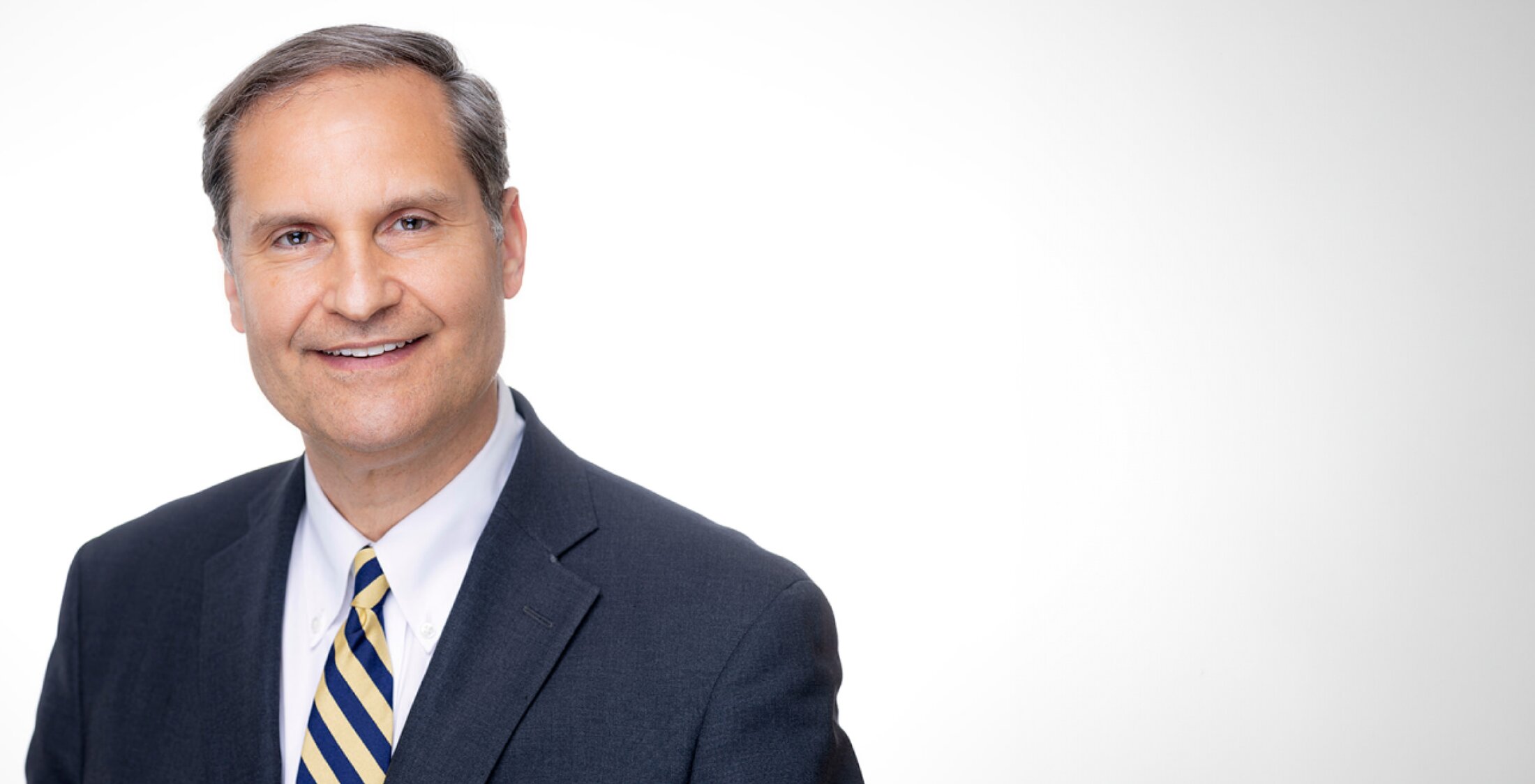Male surgeon in dark navy blazer and striped tie, professional headshot