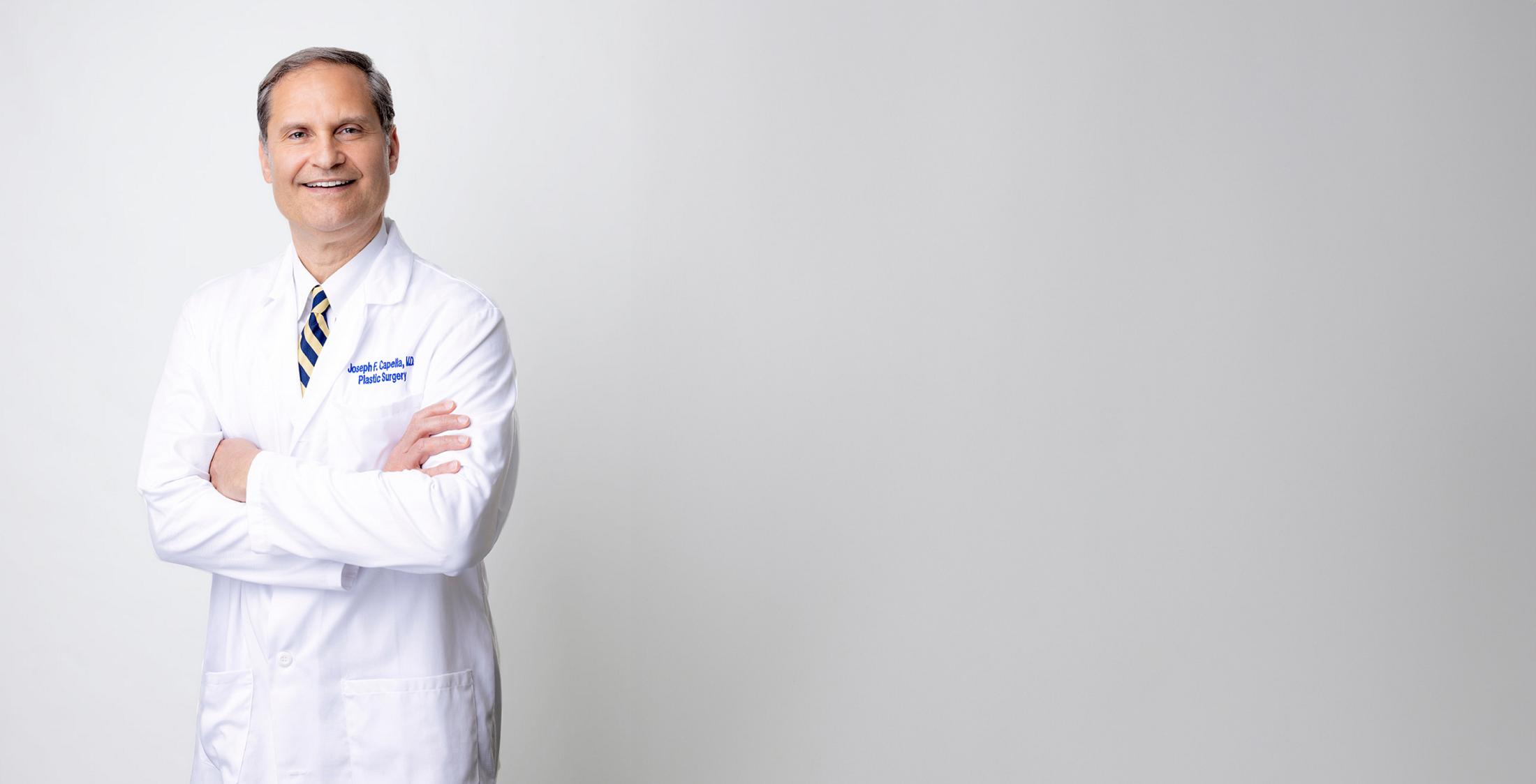 Male plastic surgeon in white coat with arms crossed, smiling at camera