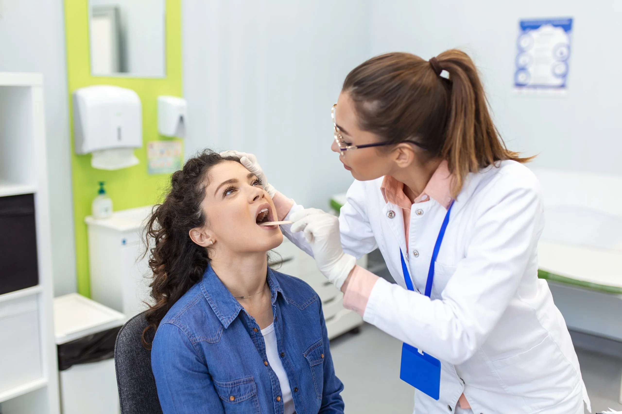 Dentist in white coat examining patient's open mouth in modern dental clinic