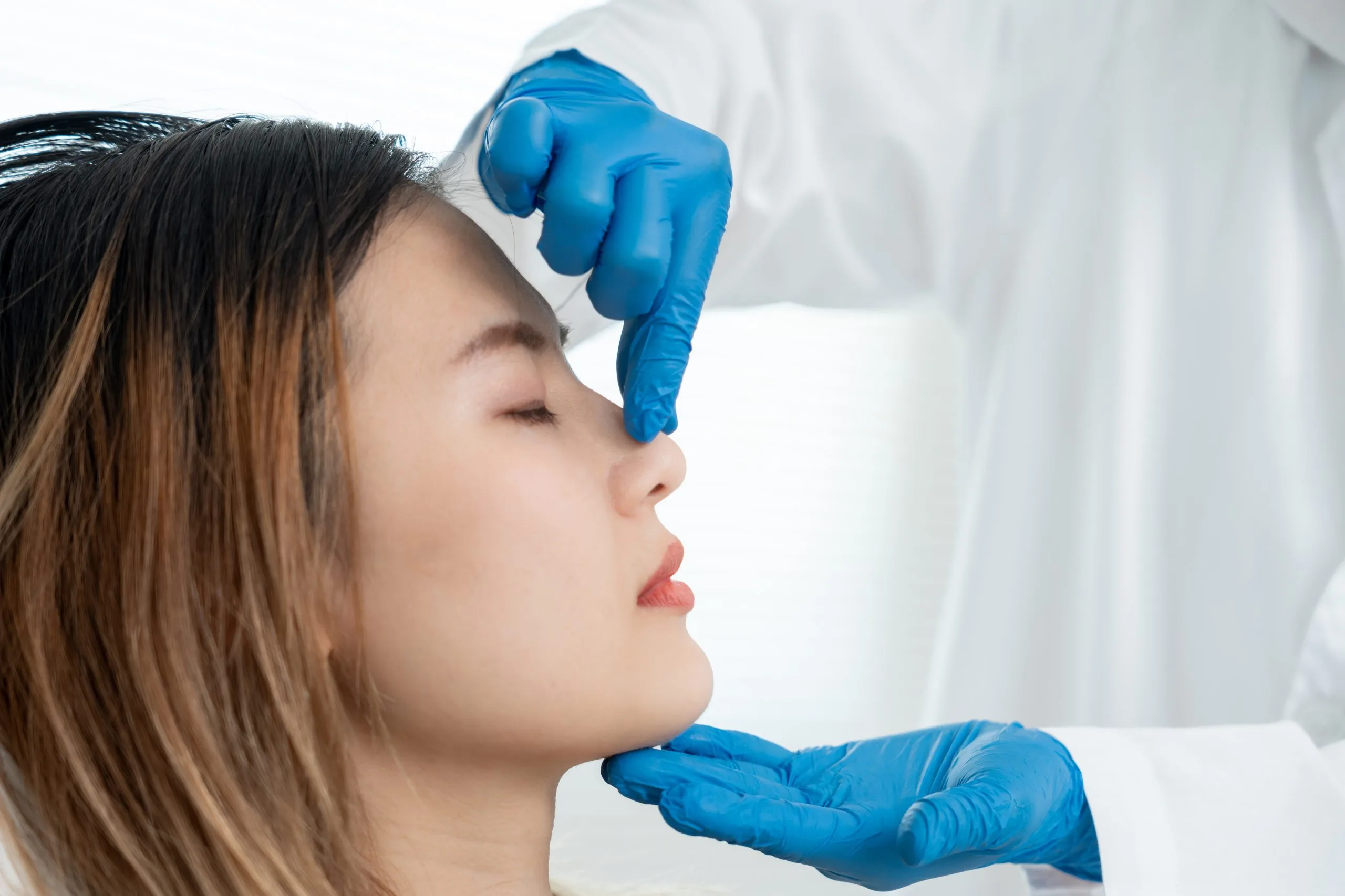 Aesthetic practitioner in blue gloves assessing woman's nose profile