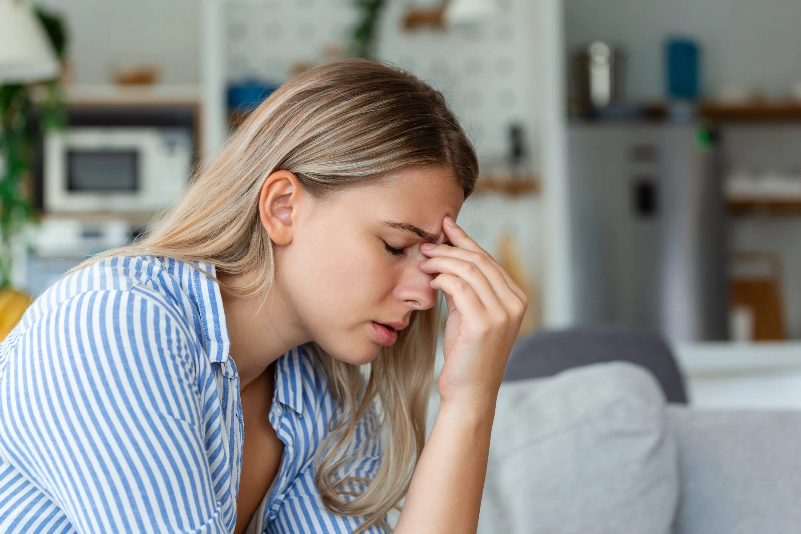Woman in blue striped shirt holding her face, appearing fatigued or experiencing discomfort in a home setting