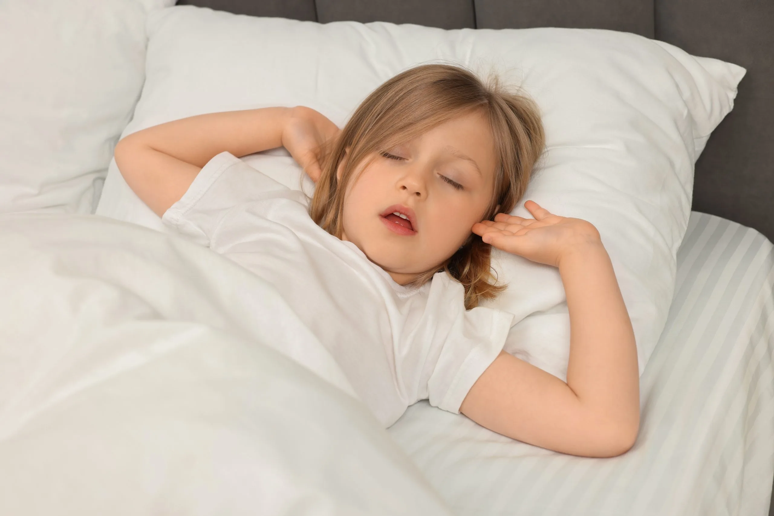 Child sleeping peacefully in bed with white bedding