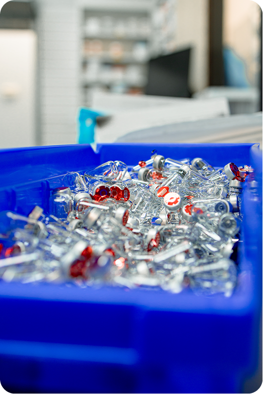 Blue bin filled with clear medication capsules and syringes with red accents