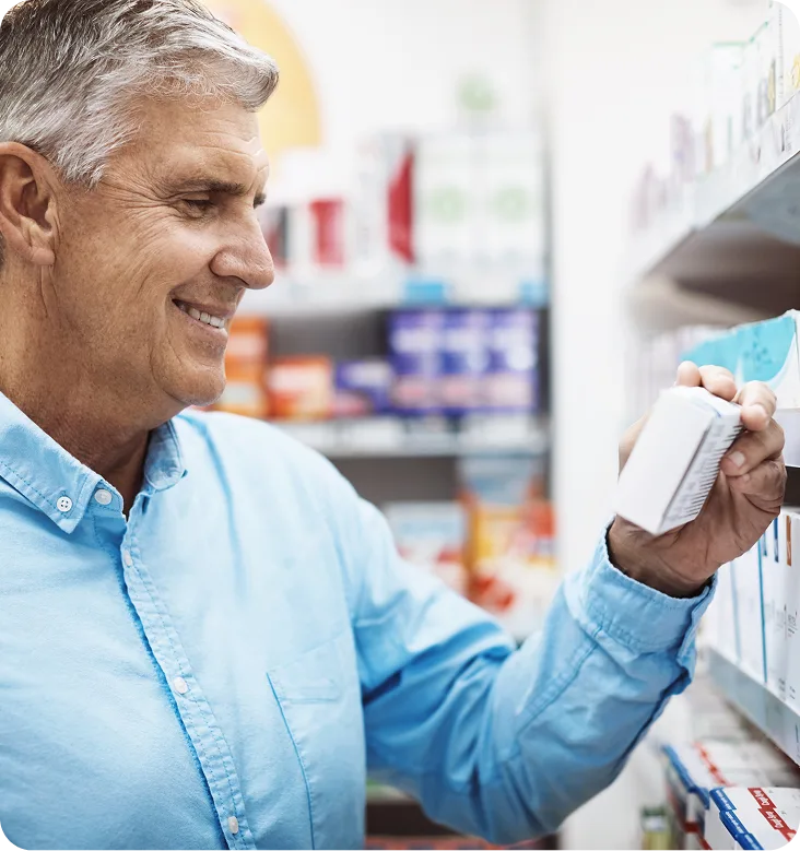 Older man in pharmacy reading medication bottle label on shelf