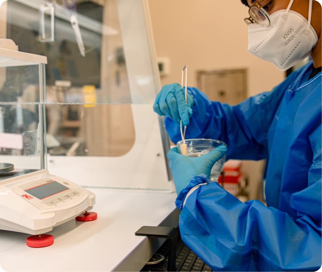 Pharmacist in blue gown and gloves preparing a compounded medication in laboratory equipment
