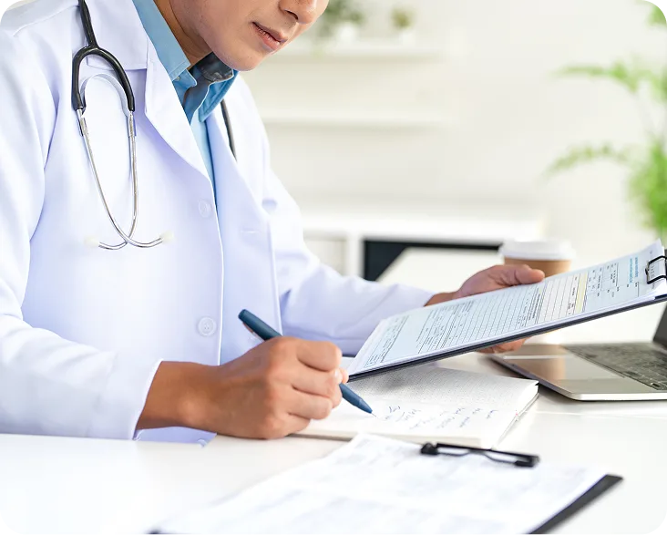 Healthcare provider in white coat with stethoscope writing on patient form at desk