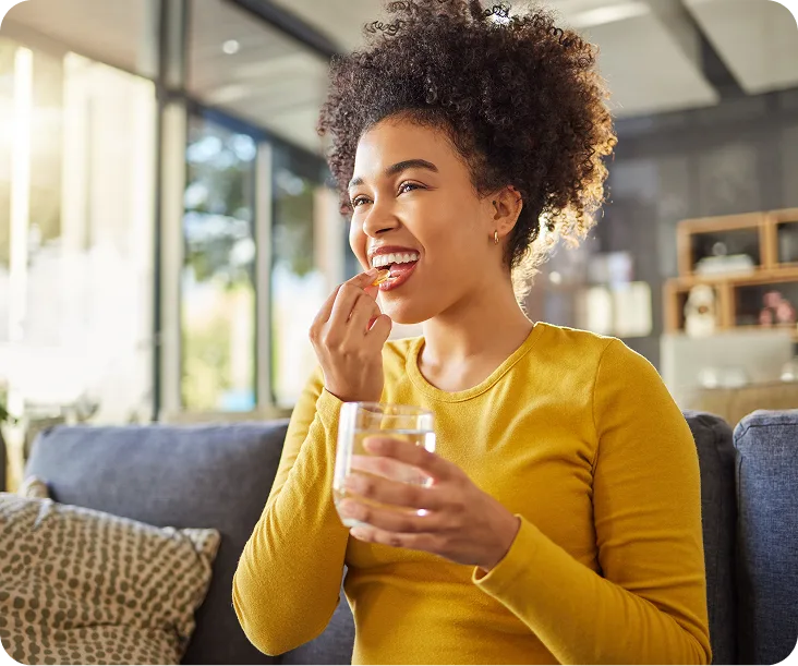 Woman in yellow shirt taking a vitamin or supplement at home