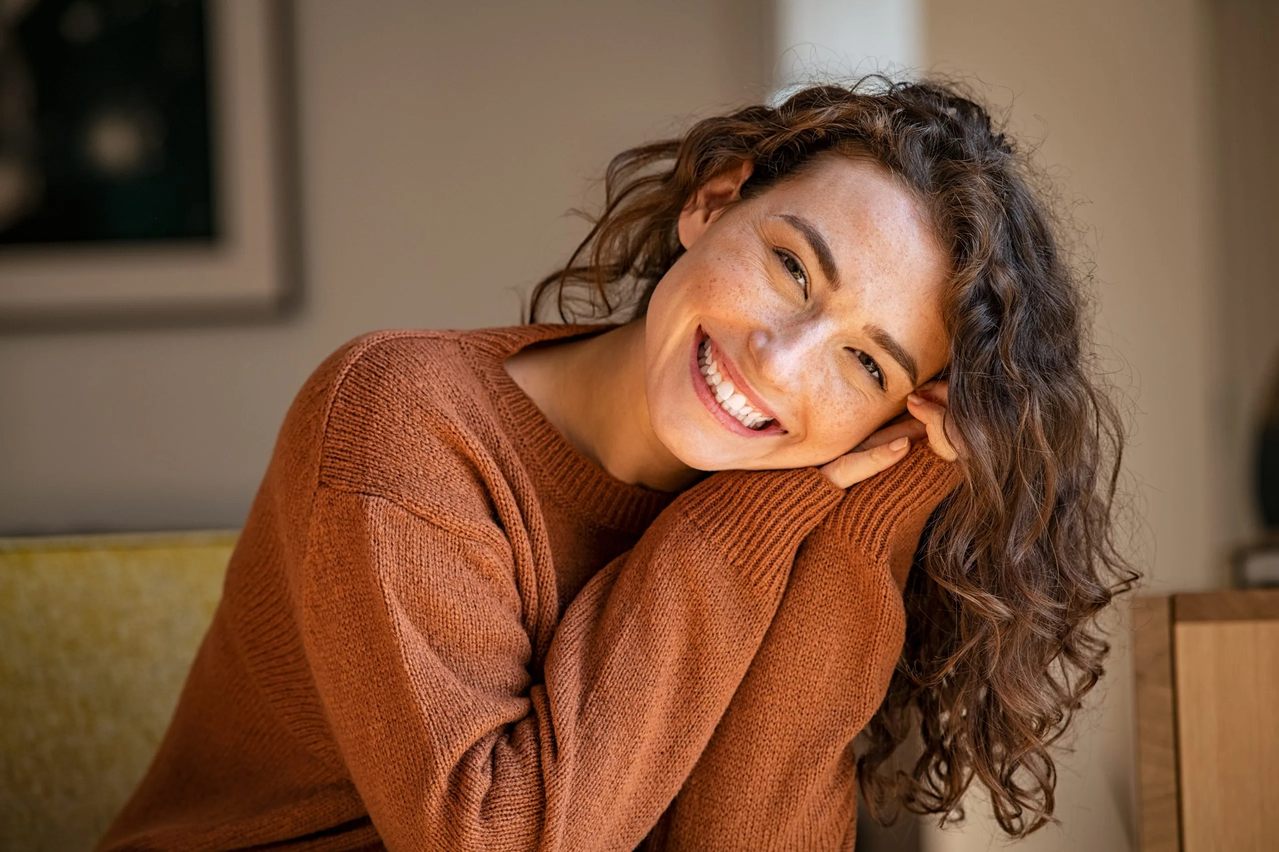 Woman smiling in rust-colored sweater, sitting on couch