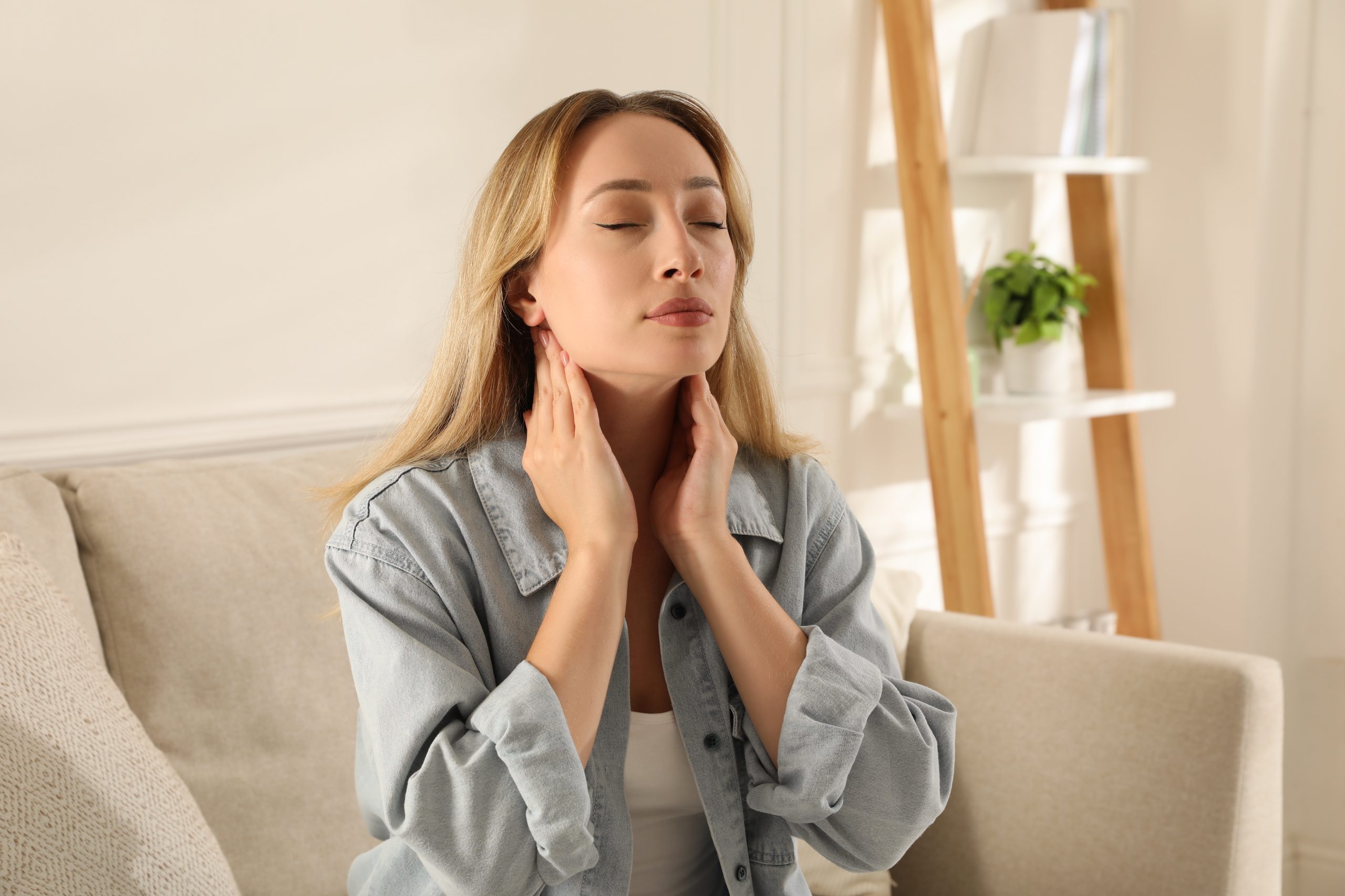 Woman touching her neck and jaw while experiencing discomfort on couch