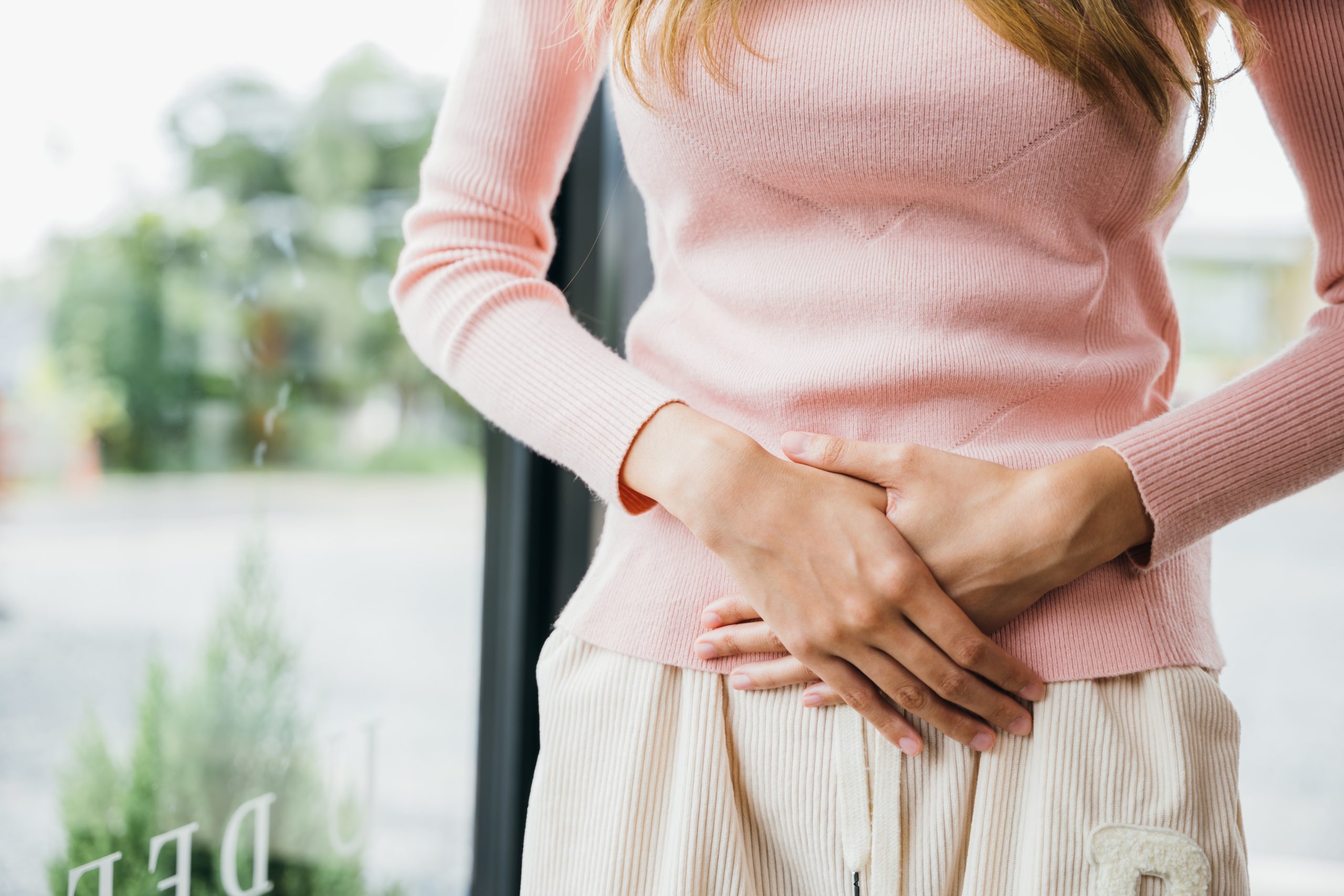 Woman in pink sweater holding her abdomen with both hands