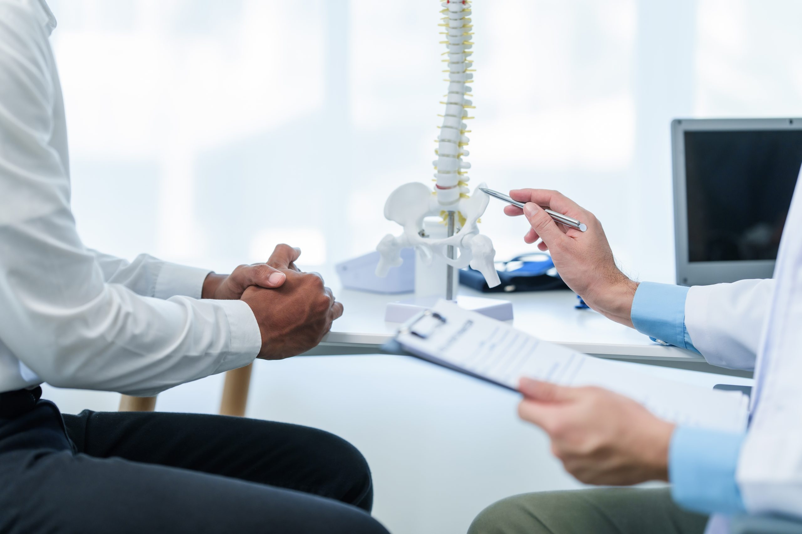 Doctor pointing to spine model while consulting with patient at desk
