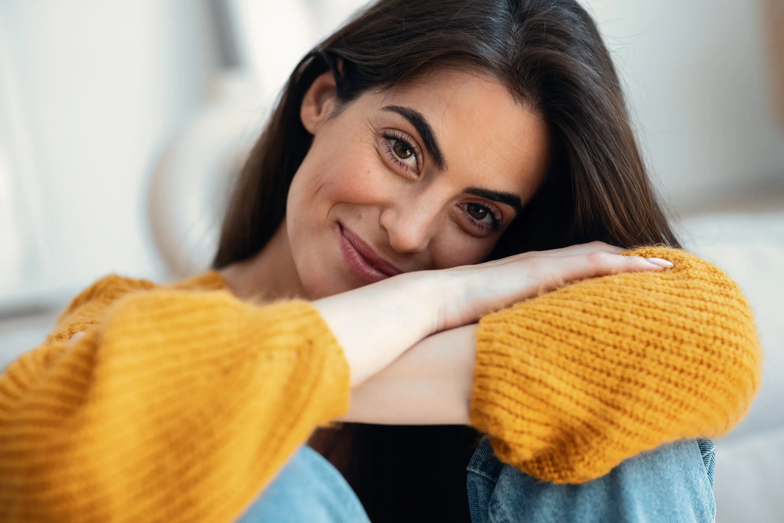 Woman in yellow sweater resting head on arms, smiling at camera