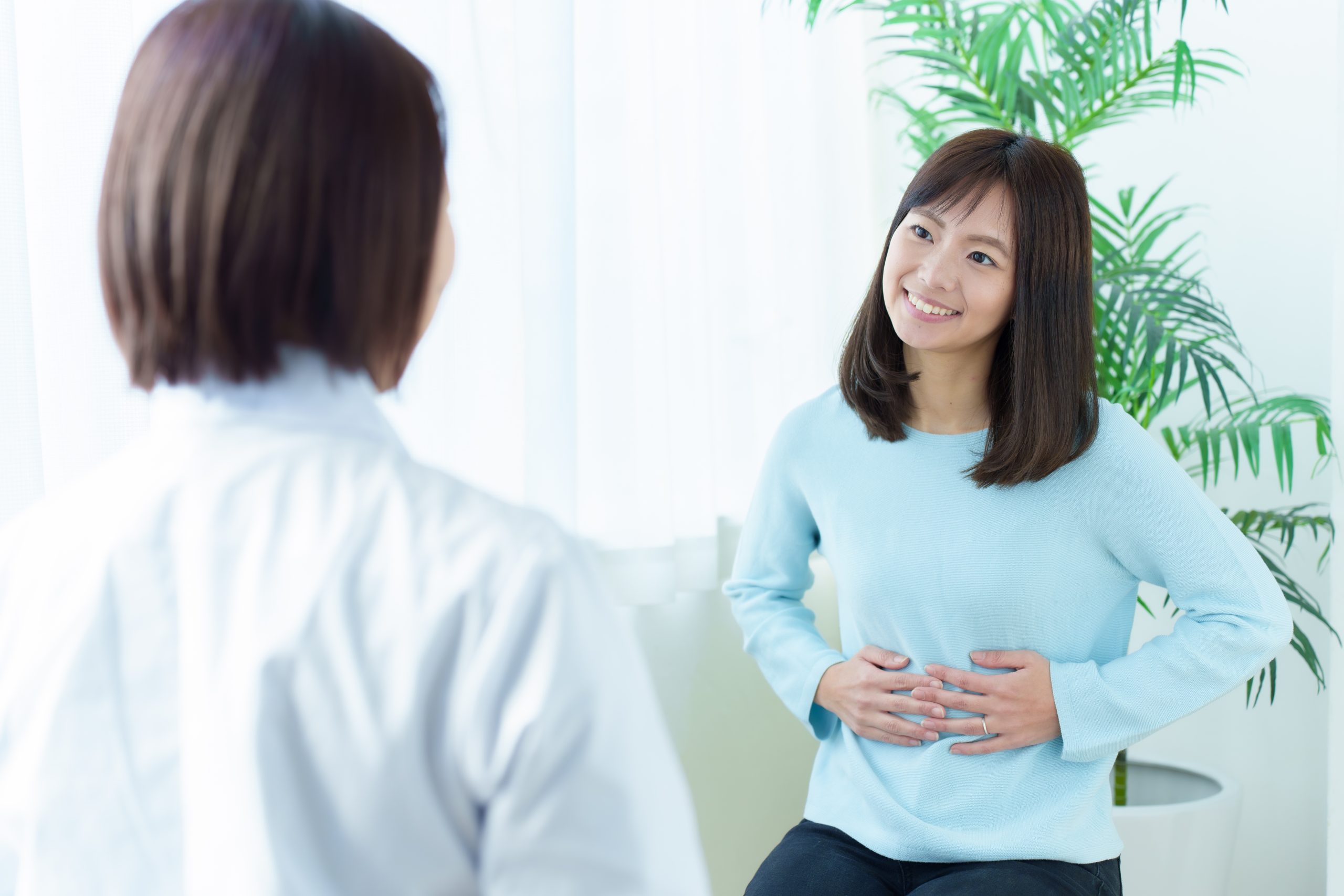 Female healthcare provider speaking with patient near indoor plant in bright office