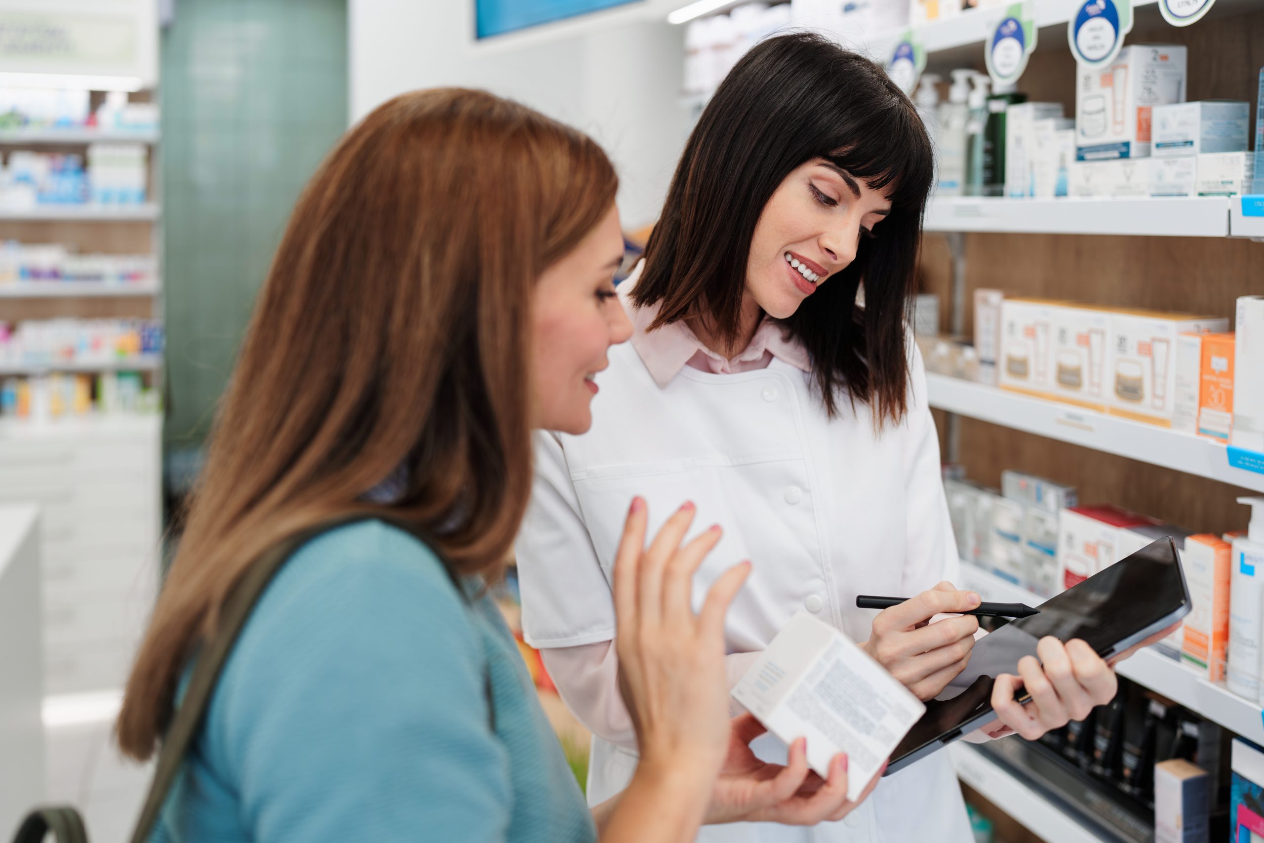 Pharmacist in white coat discusses medication with female customer in pharmacy