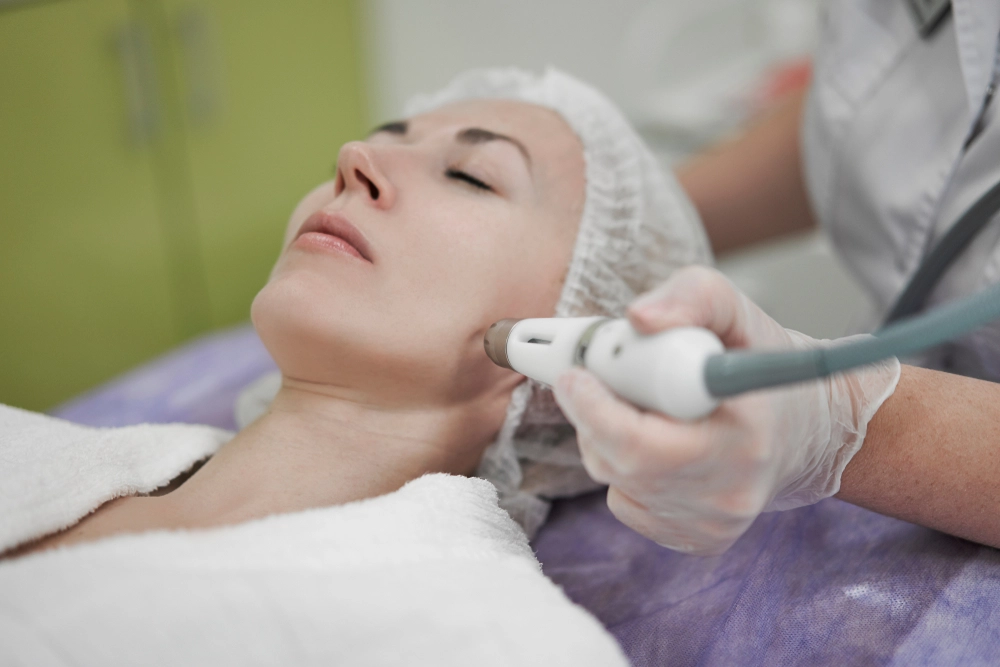 Gloved practitioner using handheld device for facial skin rejuvenation on reclining patient