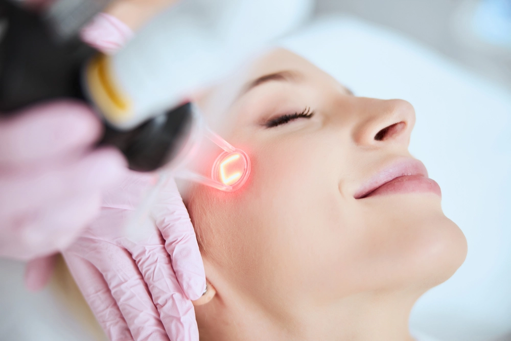 Practitioner applying red light therapy device to patient's cheek during facial treatment