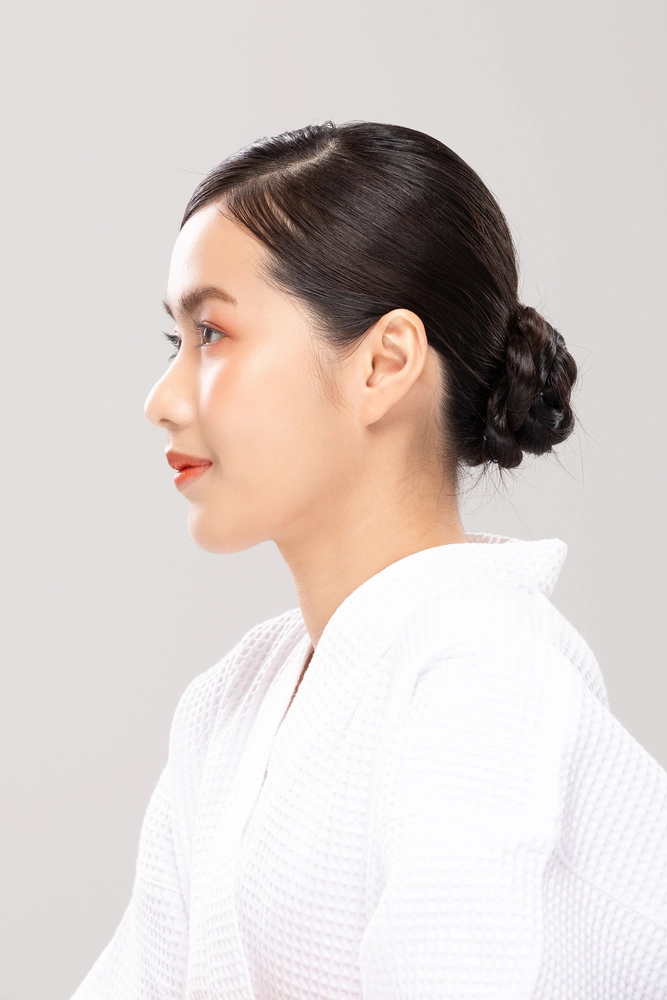 Woman in profile wearing white shirt, looking down with composed expression