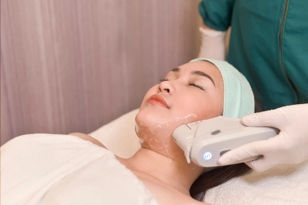 Practitioner performing ultrasound or radiofrequency skin treatment on patient's neck and jaw