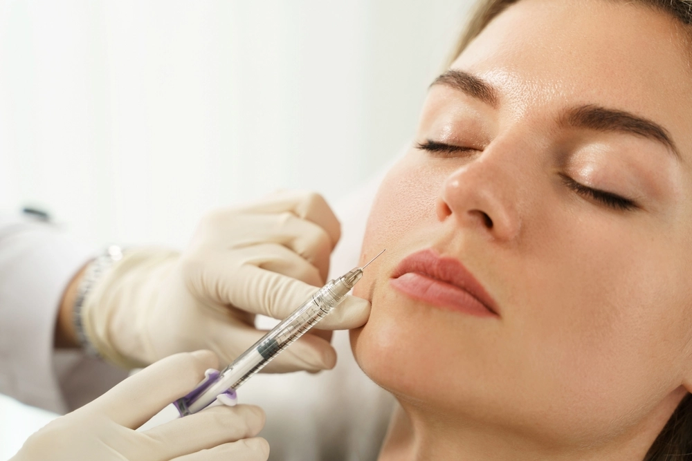 Gloved practitioner administering injectable filler treatment to patient's cheek