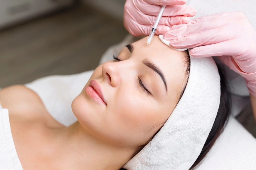 Provider in pink gloves injects filler into patient's forehead during cosmetic procedure