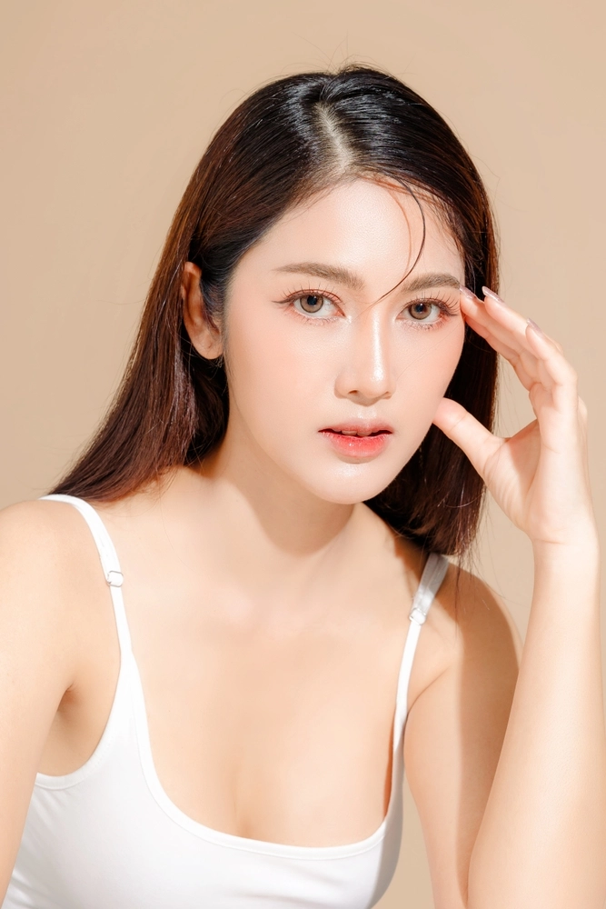 Woman with dark hair touching under eye area against neutral background
