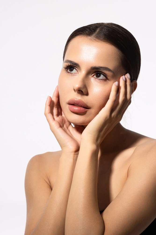 Woman with glowing skin holding her face with both hands against white background