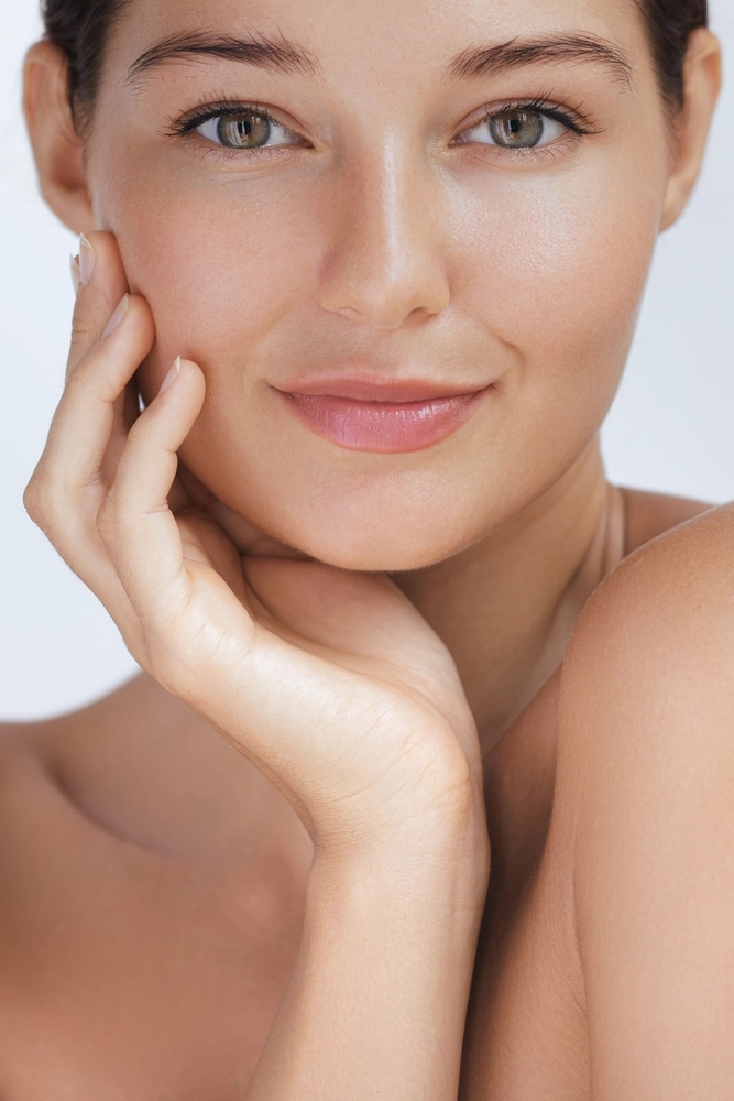 Woman touching her face and smiling at camera, displaying clear complexion