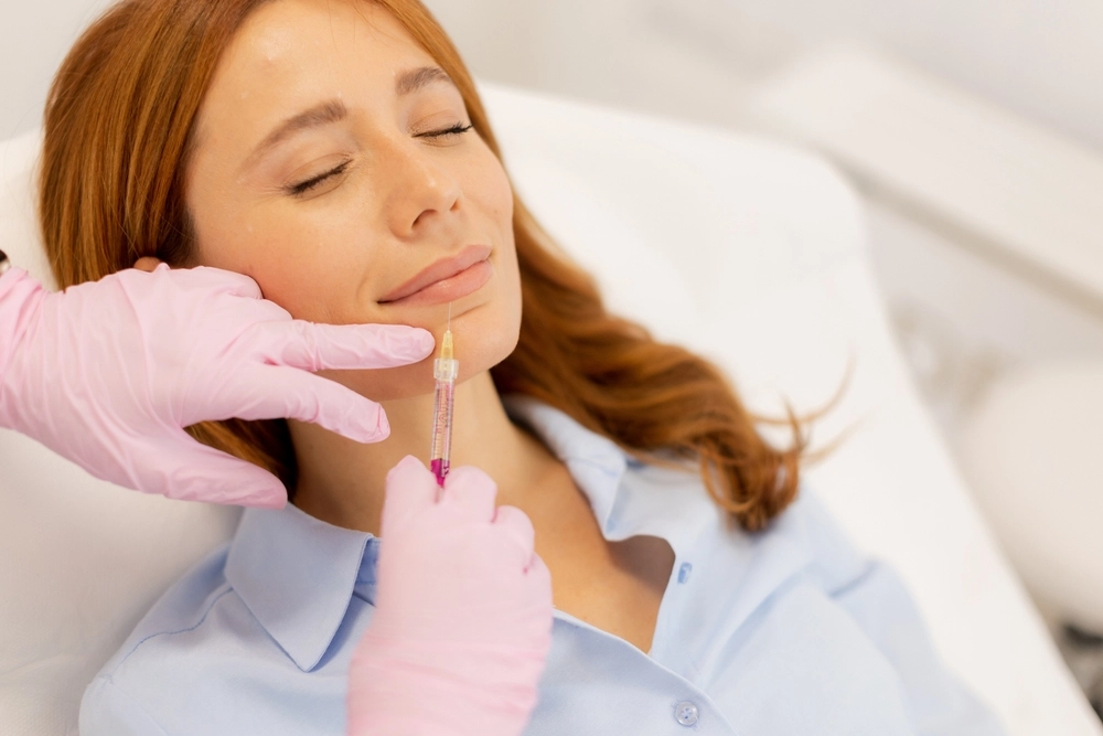 Gloved practitioner drawing liquid from syringe near patient's chin during injectable treatment